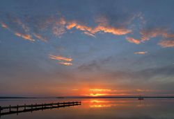 Vom Südufer aus schaut man über einen Steg in Richtung Sonnenuntergang
