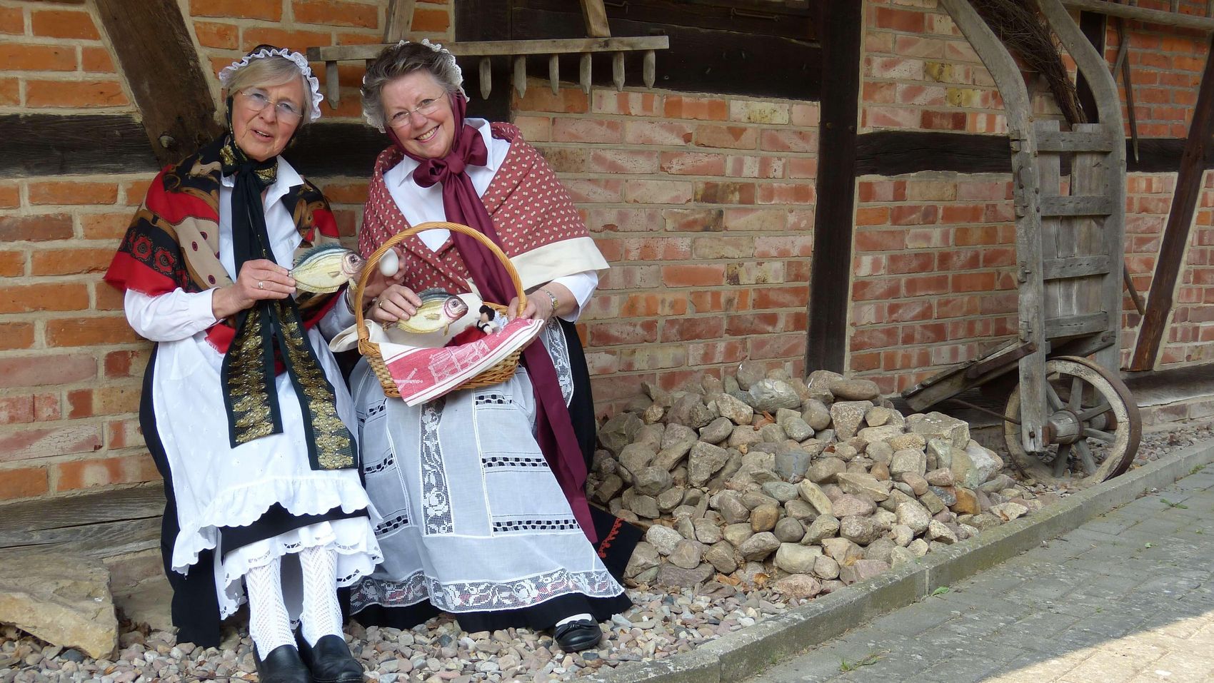 Kulinarische Orts(ver)führung Zwei Gästeführerinnen in Tracht sitzen vor der Kastenmangel in Steinhude