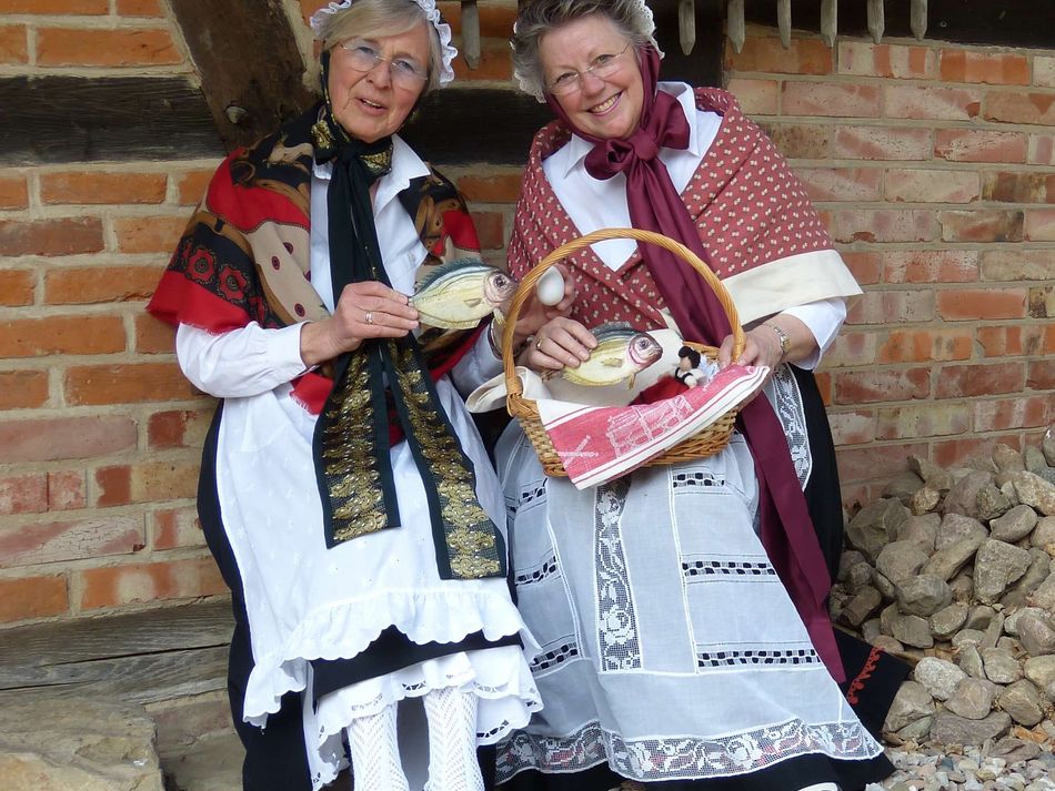 Kulinarische Orts(ver)führung Zwei Gästeführerinnen in Tracht sitzen vor der Kastenmangel in Steinhude