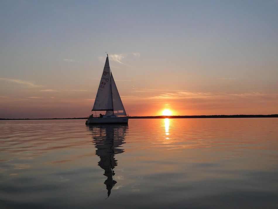 Segelboot im Sonnenuntergang Ein Segelboot fährt auf glatten Wasser unter Segeln der Sonne entgegen