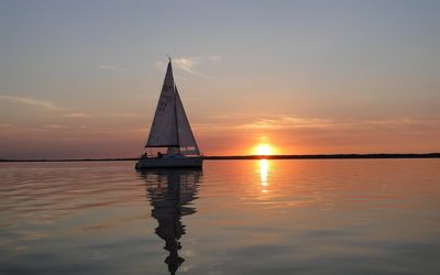 Segelboot im Sonnenuntergang Ein Segelboot fährt auf glatten Wasser unter Segeln der Sonne entgegen