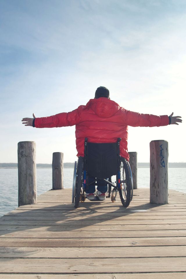 Rollstuhlfahrer auf Steg Rollstuhlfahrer genießt auf einem Steg den Blick über das Wasser