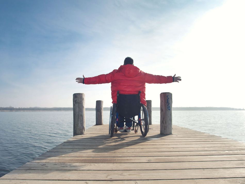 Rollstuhlfahrer auf Steg Rollstuhlfahrer genießt auf einem Steg den Blick über das Wasser