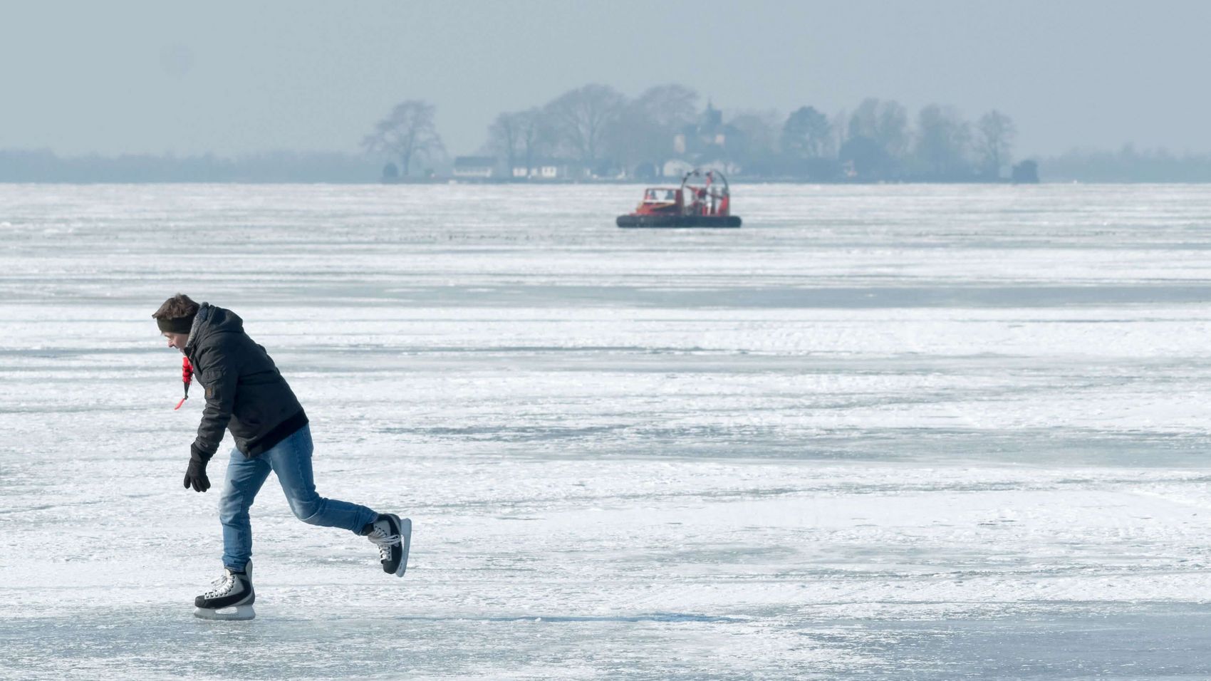 Schlittschuhlläufter auf dem Steinhuder Meer Auf dem zugefrorenen Steinhuder Meer ist ein Mann mit Schlittschuhen unterwegs. Im Hintergrund sieht man die Insel Wilhelmstien und das Hovercraft der Feuerwehr Steinhude.