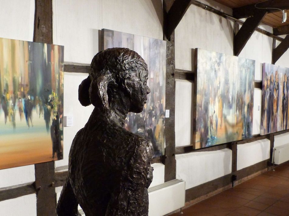 Ausstellung in der Kunstscheune Steinhude Eine Bronzefigur schaut an vielen Bilder die in der Kunstscheune Steinhude hängen vorbei