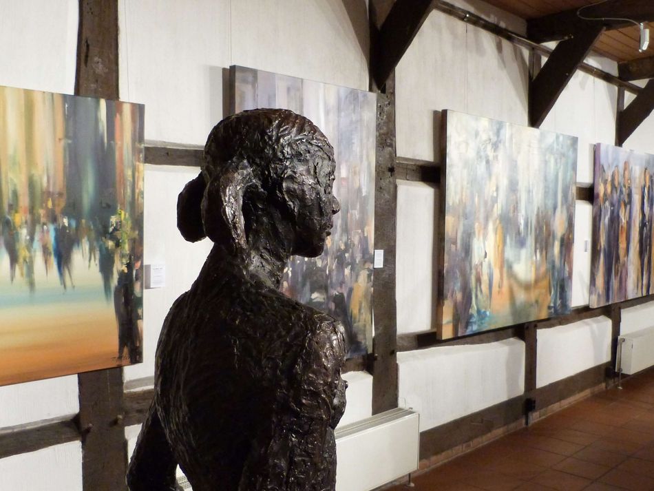 Ausstellung in der Kunstscheune Steinhude Eine Bronzefigur schaut an vielen Bilder die in der Kunstscheune Steinhude hängen vorbei