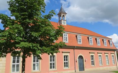 Die historische Bäderanlage Romantik Bad Rehburg. Das Gebäude im rosaton steht unter einem blauen bewölkten Himmel.