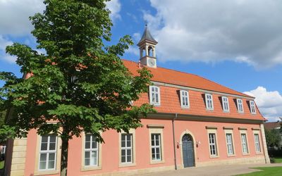 Romantik Bad Rehburg Die historische Bäderanlage Romantik Bad Rehburg. Das Gebäude im rosaton steht unter einem blauen bewölkten Himmel.