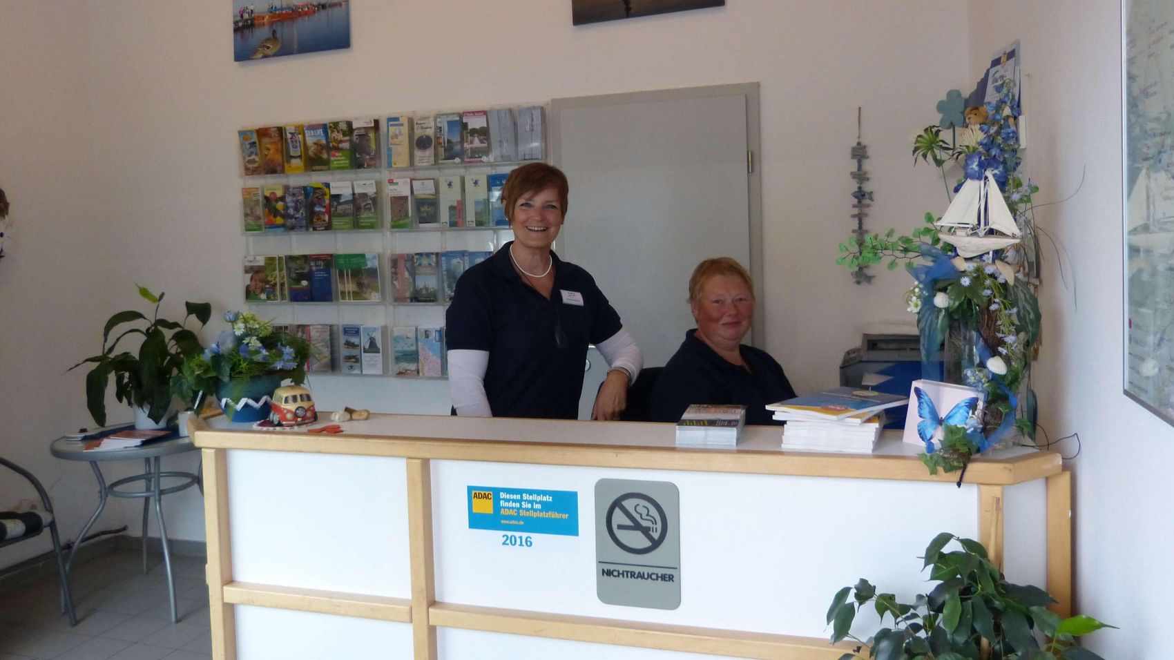 Womo Steinhude Counter Zwei Mitarbeiterinnen des Wohnmobilstellplatzes Steinhude heißen die Gäste hinter dem Counter mit einem fröhlichen Lächeln herzlich willkommen